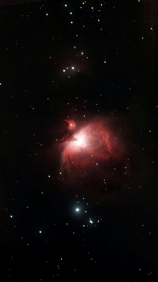 The Orion Nebula: a glowing red cloud of gas with a bright white core, surrounded by stars on a dark sky, with the smaller round M43 just above it, a faint nebula near the top and a bright star with a small cluster below.
