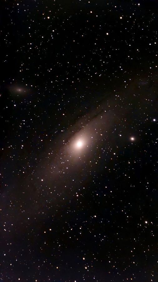 The Andromeda Galaxy: a bright yellow-white core inside a faint, tilted oval of dust and stars, with the small fuzzy satellite galaxy M110 near the top left, on a dark field full of stars.